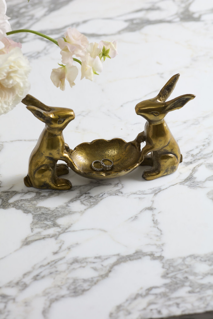 Best Bunnies Dish Stand, an accent decor piece featuring two brass bunnies holding a small dish with rings on a marble surface.