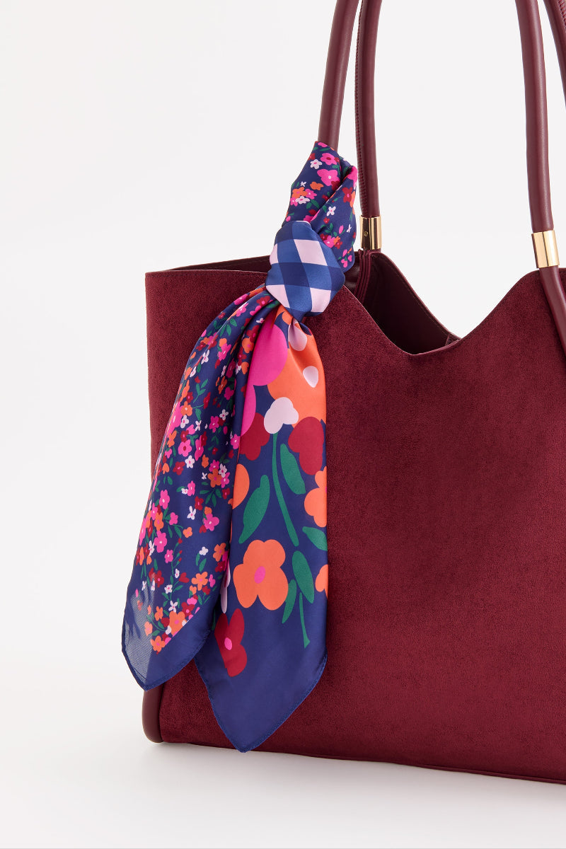 Close-up of Shiraleah Navy Floral Square Scarf with pink, orange, and blue patterns, tied to a burgundy handbag.