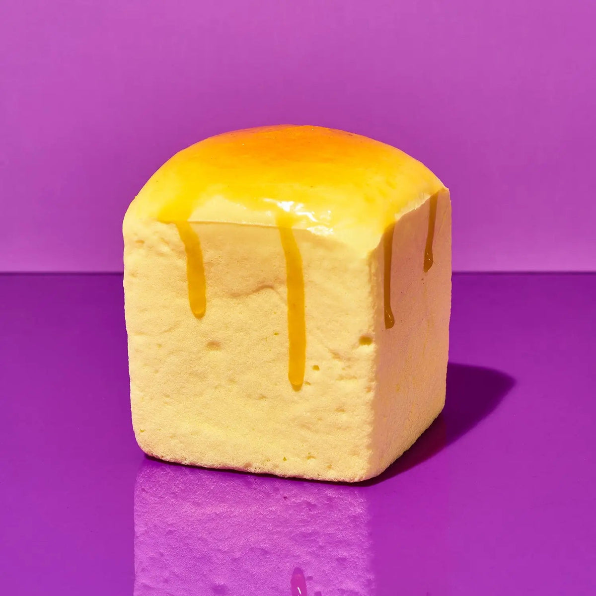 Grabie Squishy - Melty Butter Cube, a soft yellow cube toy with shiny yellow drips like melted butter, on a purple background.
