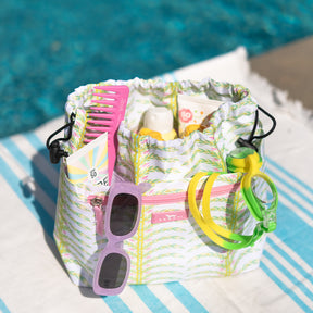 SCOUT Glam Squad Makeup Bag with pool essentials: sunscreen, sunglasses, comb, and goggles, by a pool.