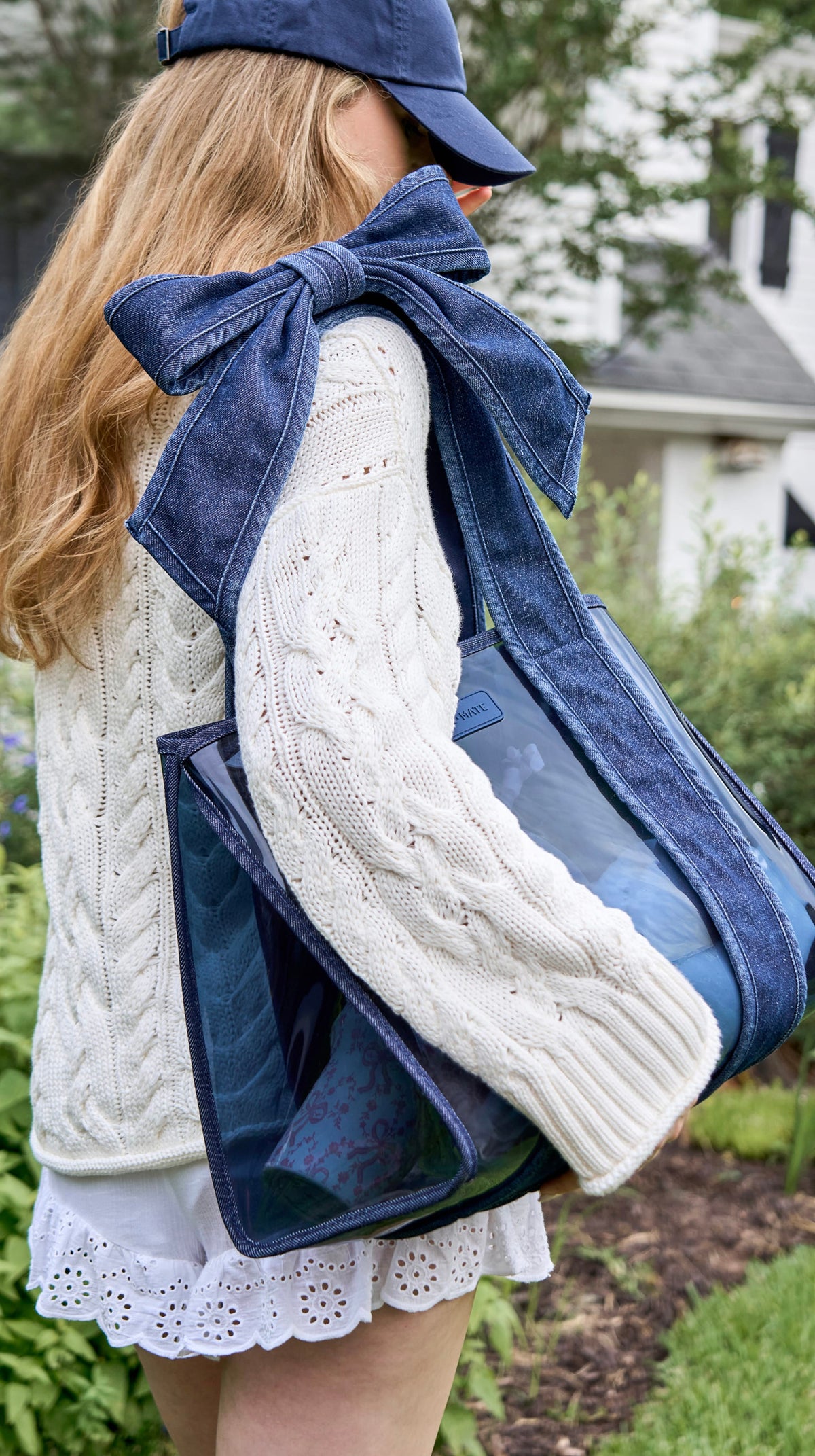 Case-Mate Jelly Tote with Phone Pouch and large Denim Bow, carried by a person in a white cable knit sweater and blue cap.